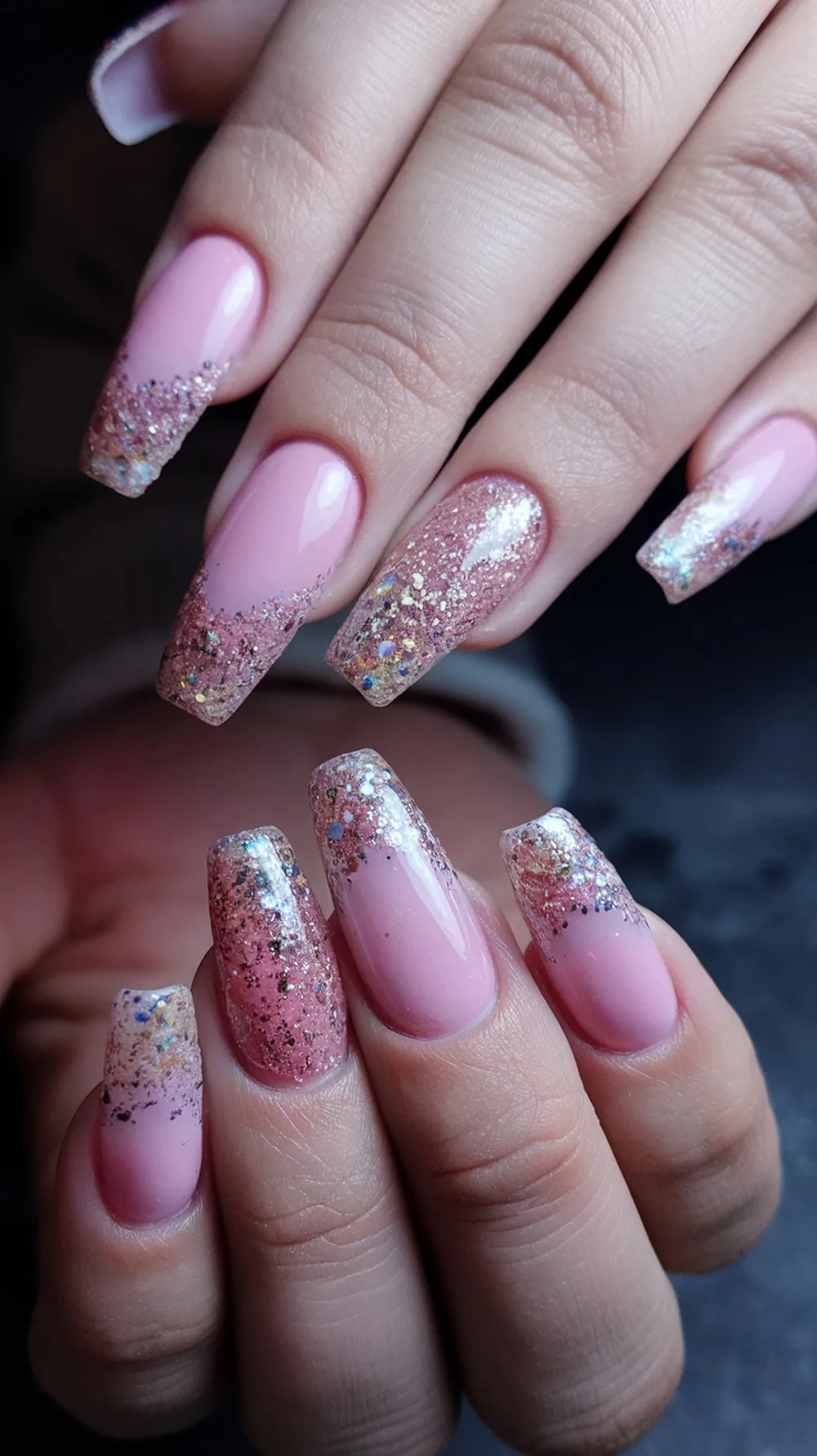A close-up of hands showing glitter gradient nails with a pink base and sparkling tips.