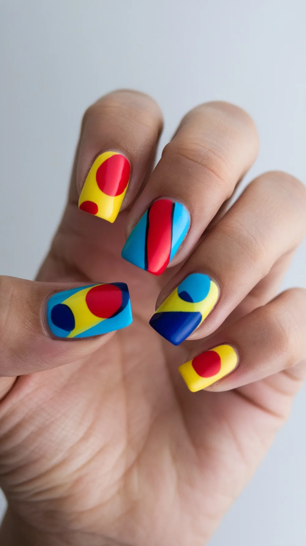 Nail art featuring bold geometric shapes in red, blue, and yellow.